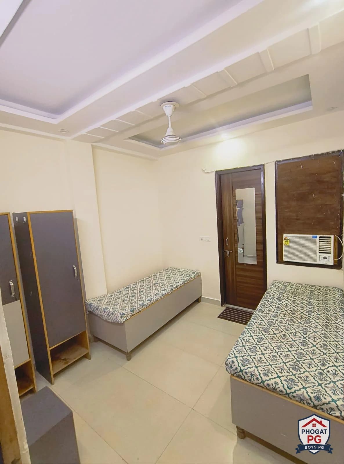 Two single beds with wardrobes, a window AC and ceiling fan in a Phogat PG room