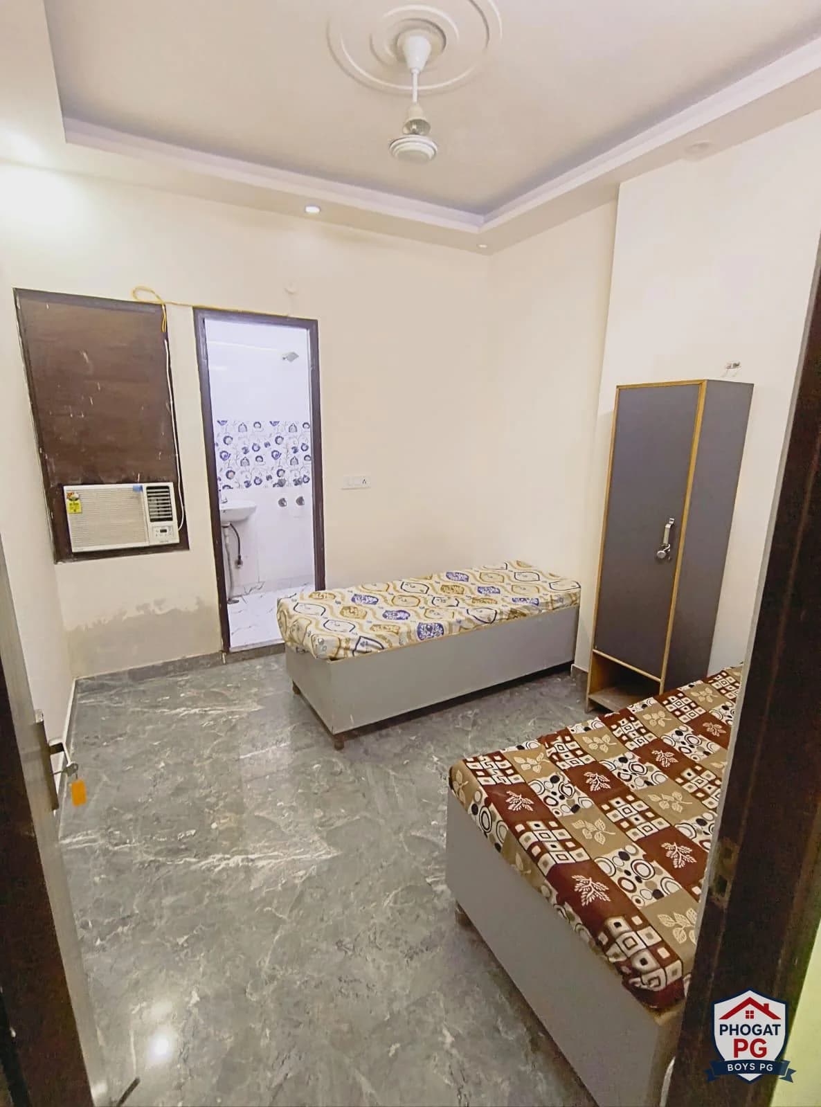 Two single beds with wardrobes, a window AC and bathroom doorway in a Phogat PG room