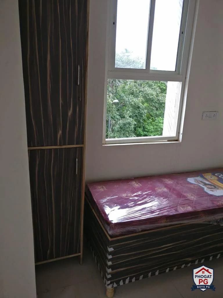 Bed and wardrobe beside a window in a Phogat PG room
